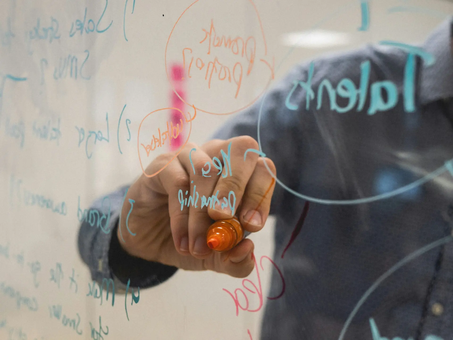 Person writing colorful ideas and concepts on a transparent board with a marker, representing innovation, creativity, and planning.